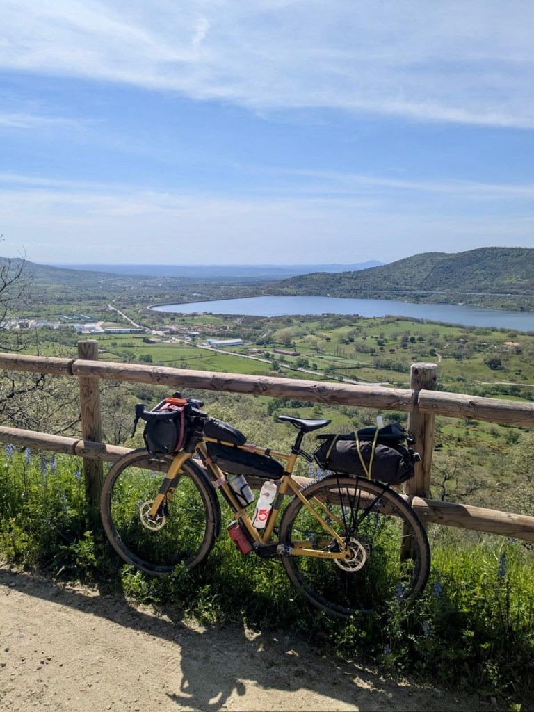Fully loaded touring bike overlooking a scenic valley and lake in Spain during a solo bikepacking trip.